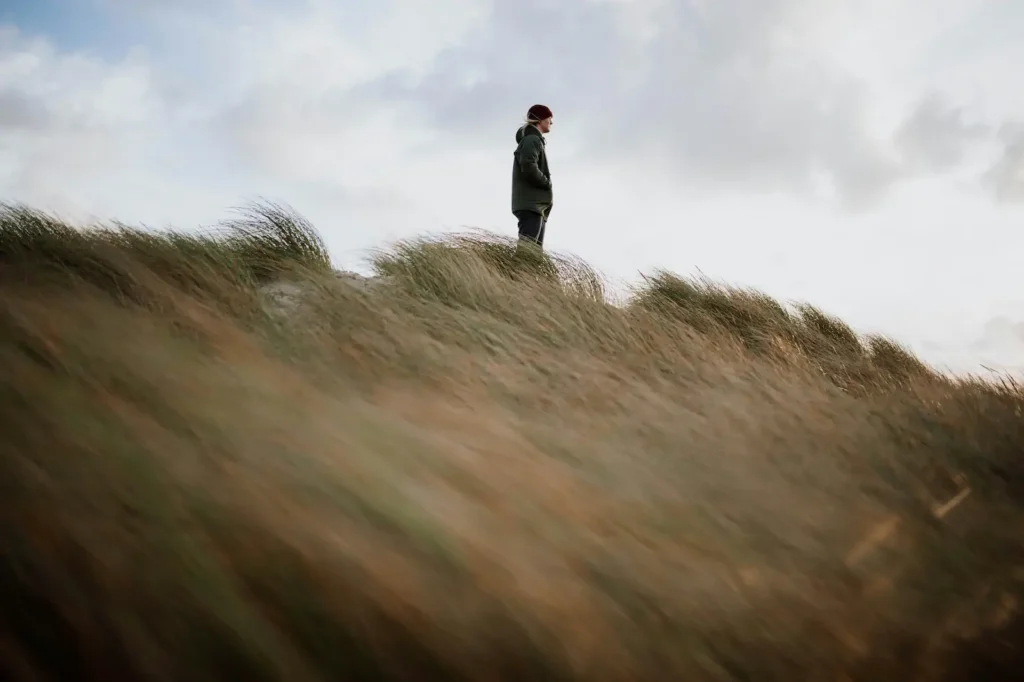 Person standing on windy hilltop with grass