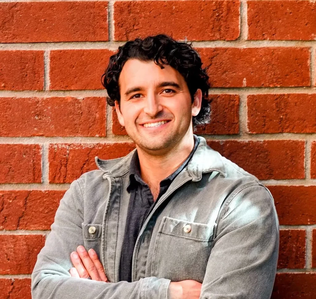 Smiling man with curly hair wearing jacket against brick wall