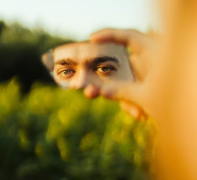 Close-up of eyes framed by hands and greenery